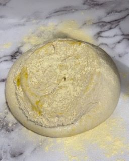 Un pezzo di pasta è appoggiato su una superficie di marmo ricoperta di farina.