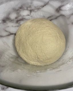 Una palla di pasta è appoggiata su una ciotola di vetro.