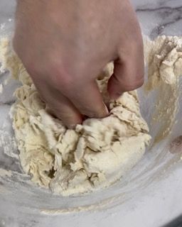 Una persona sta impastando l'impasto in una ciotola di vetro.