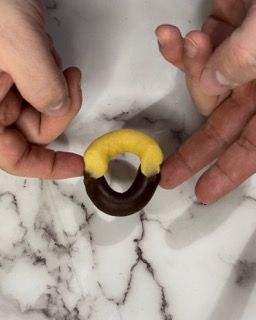 Una persona tiene in mano una ciambella al cioccolato ricoperta di glassa gialla.