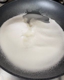 Una padella piena di zucchero bianco e un cucchiaio dentro.