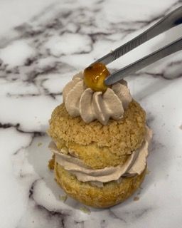 Un primo piano di un pasticcino con panna montata e una ciliegia sopra.