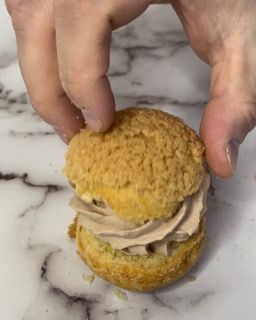 Una persona tiene in mano un piccolo dolcetto con sopra della panna montata.