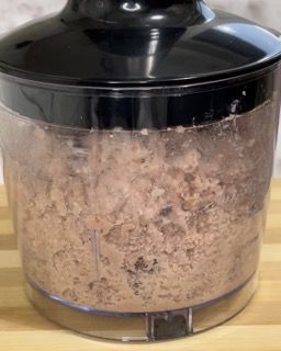 Primo piano di un robot da cucina pieno di cibo su un tagliere.