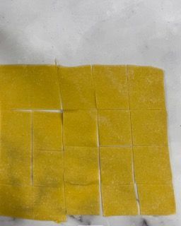 Un pezzo di pasta gialla viene tagliato a quadrati su un tavolo.