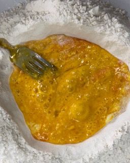 Una forchetta conficca un liquido giallo in una ciotola di farina.