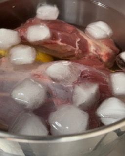 Un grosso pezzo di carne viene cucinato in una pentola con acqua e cubetti di ghiaccio.