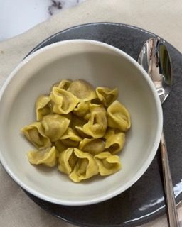 Una ciotola di pasta è appoggiata su un piatto accanto a un cucchiaio