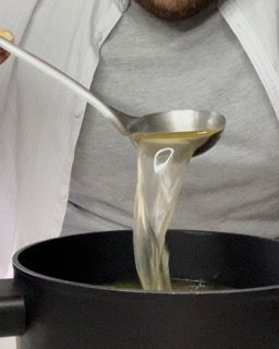 Una persona versa del liquido da un mestolo in una pentola