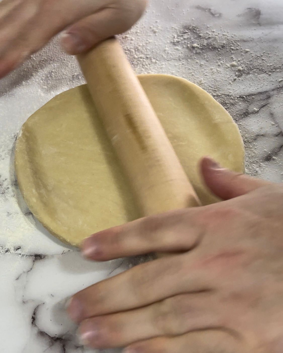 Una persona sta stendendo la pasta con un mattarello di legno.
