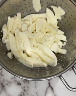 Sul tavolo c'è uno scolapasta pieno di patate tritate.