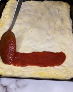 Si usa un cucchiaio per spalmare la salsa di pomodoro sull'impasto della pizza.