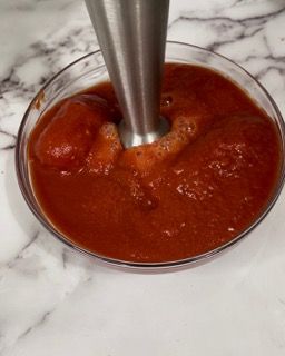 Una ciotola di salsa di pomodoro viene frullata con un frullatore.