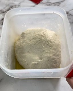 Una persona tiene in mano un contenitore di plastica pieno di impasto.