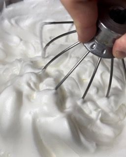 Una persona tiene una frusta sopra una ciotola di panna montata.