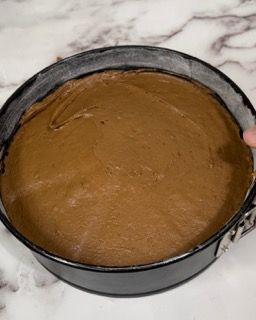 Una persona tiene in mano una teglia piena di impasto per torta al cioccolato.