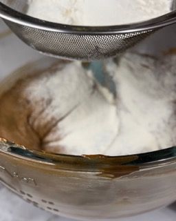 Una persona sta setacciando la farina in una ciotola con l'impasto.