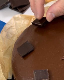 Una persona tiene in mano un pezzo di cioccolato sopra una torta al cioccolato.