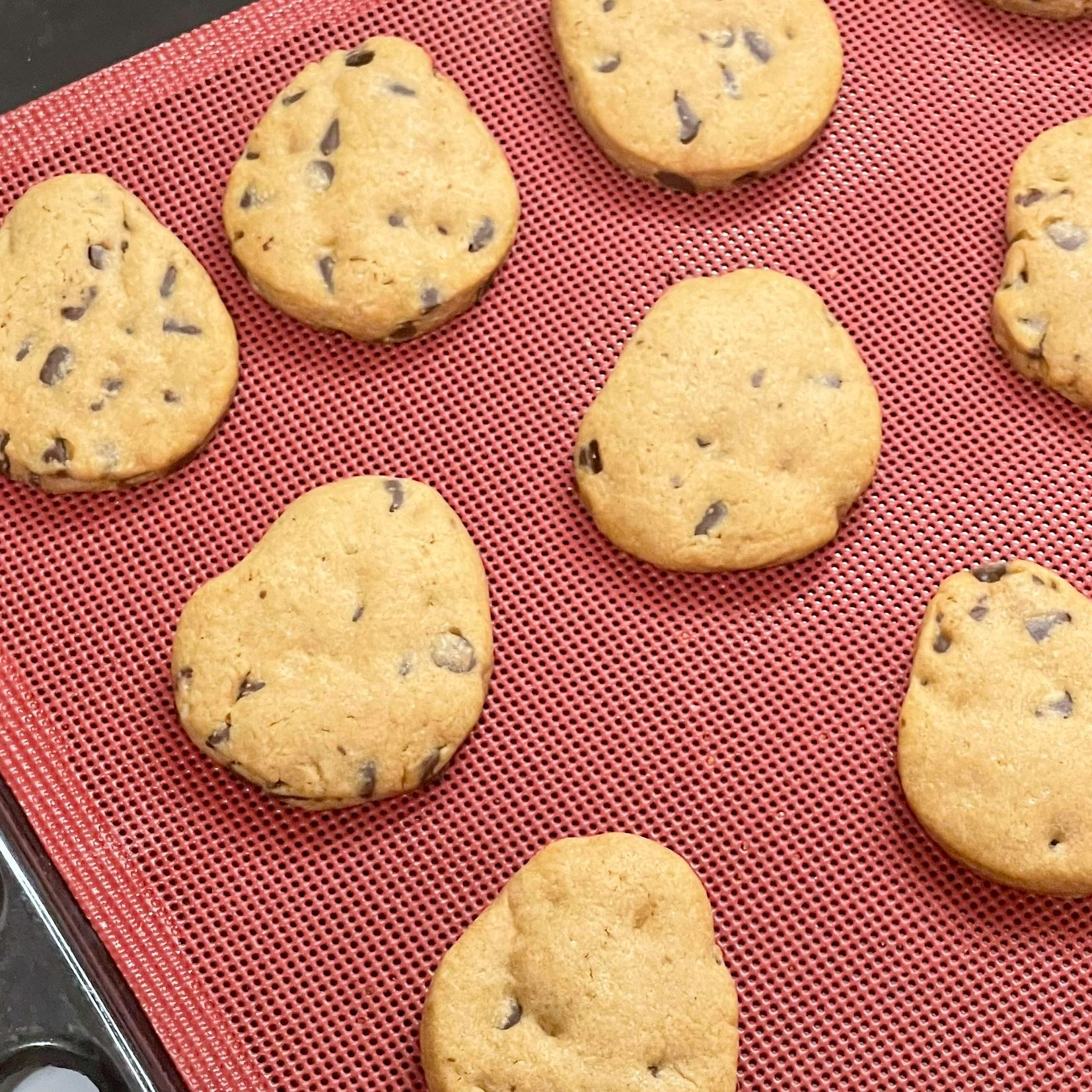 Un mucchio di biscotti con gocce di cioccolato sono appoggiati su una tovaglietta rossa.