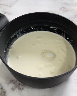 Una padella nera piena di liquido bianco è appoggiata su un tavolo.