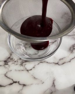 Una ciotola di salsa viene versata attraverso un colino su un tavolo.