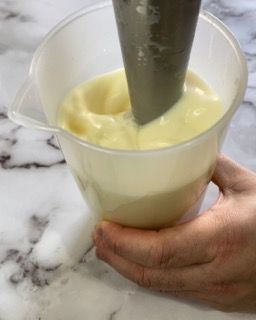 Una persona tiene in mano un misurino pieno di un liquido giallo.