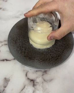 Una persona tiene in mano un bicchiere di maionese su un piatto.