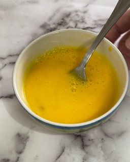 Una ciotola di liquido giallo con una forchetta dentro su un tavolo.