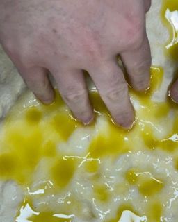 ani che distribuiscono la salamoia sulla focaccia in teglia