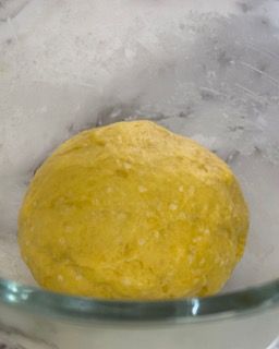 Una palla di pasta gialla è posta in una ciotola di vetro.