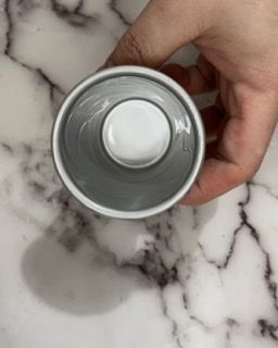 Una persona tiene in mano una tazza grigia con un coperchio bianco su una superficie di marmo.