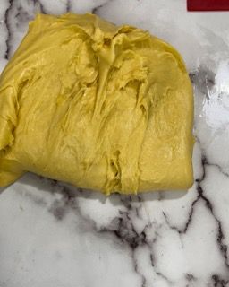 Un pezzo di pasta gialla è appoggiato su una superficie di marmo.