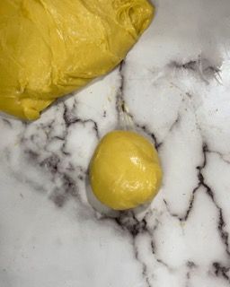 Una palla di pasta gialla è appoggiata su un bancone di marmo accanto a un sacchetto di pasta.