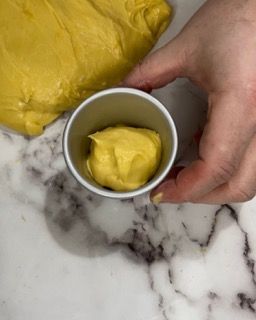 Una persona tiene in mano una tazza di salsa gialla su un tavolo.