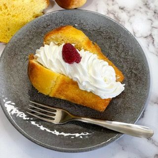 Una fetta di torta con panna montata e un lampone su un piatto con una forchetta