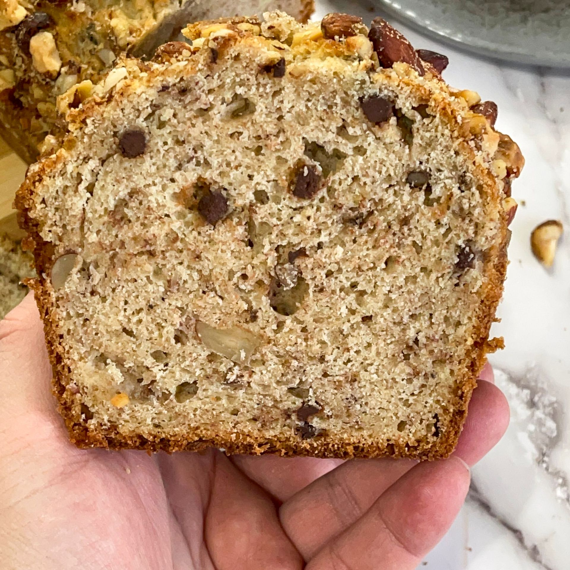 Una persona tiene in mano una fetta di pane alla banana con gocce di cioccolato.