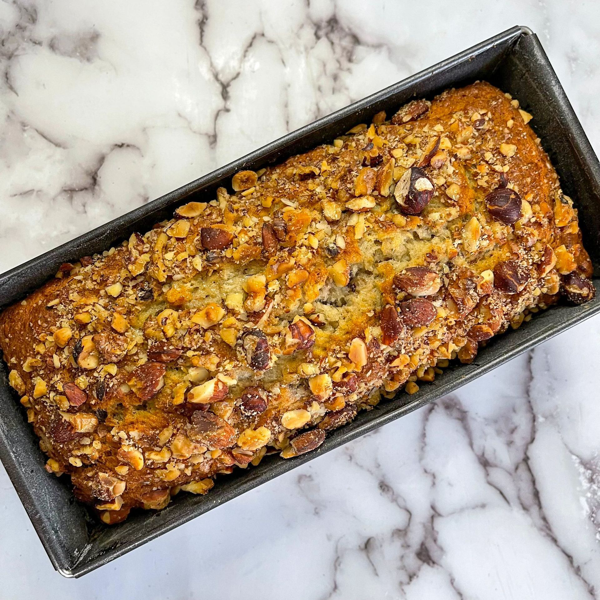 Una pagnotta di pane alle banane con noci e gocce di cioccolato in una padella su un tavolo.