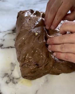 Una persona tiene in mano un pezzo di pasta al cioccolato su un tavolo.