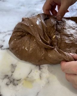 Una persona tiene in mano un pezzo di pasta al cioccolato su un tavolo.