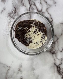 Una ciotola di vetro piena di gocce di cioccolato e panna montata su una superficie di marmo.