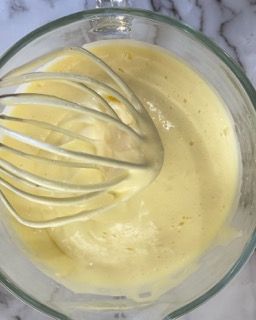 Si usa una frusta per mescolare un liquido giallo in una ciotola di vetro.