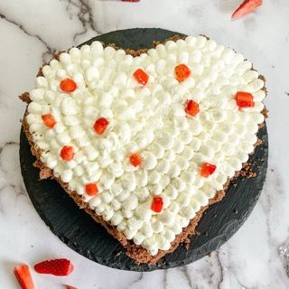 Una torta a forma di cuore con panna montata e fragole sopra