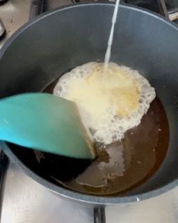 Una spatola verde versa del liquido in una padella.