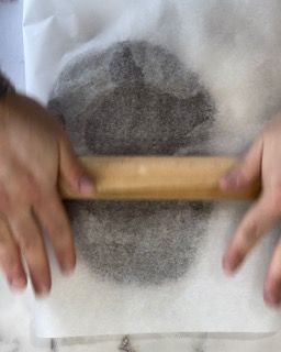 Una persona sta stendendo un pezzo di pasta con un mattarello di legno.