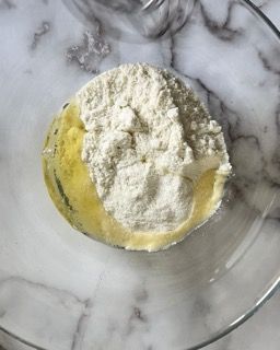 Una ciotola di vetro piena di farina e olio su una superficie di marmo.