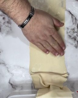 Una persona tiene in mano un pezzo di pasta su un tavolo.