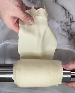 Una persona sta stendendo un pezzo di pasta su un mattarello.