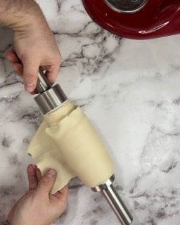 Una persona tiene in mano un pezzo di impasto accanto a un'impastatrice.