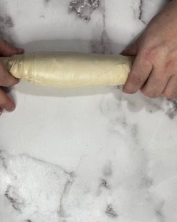 Una persona sta stendendo un pezzo di pasta con un mattarello.