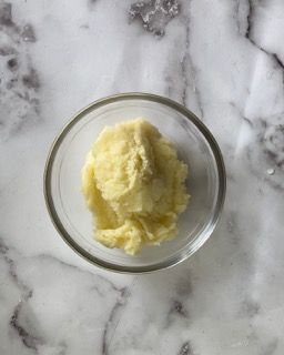 Una ciotola di vetro piena di purè di patate su una superficie di marmo.